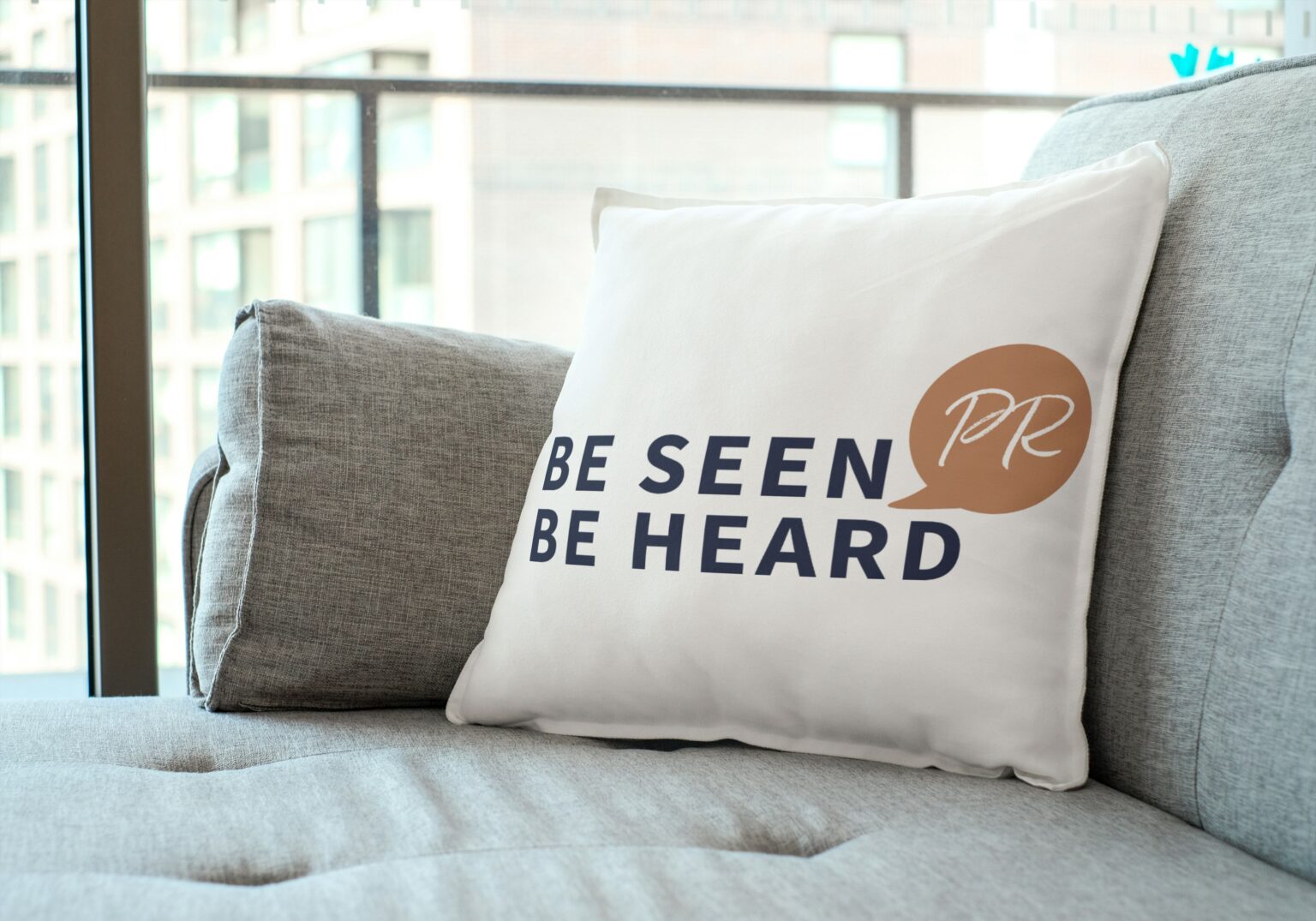 Cushion with Be Seen Be Heard PR logo on it, sitting upon a sofa.